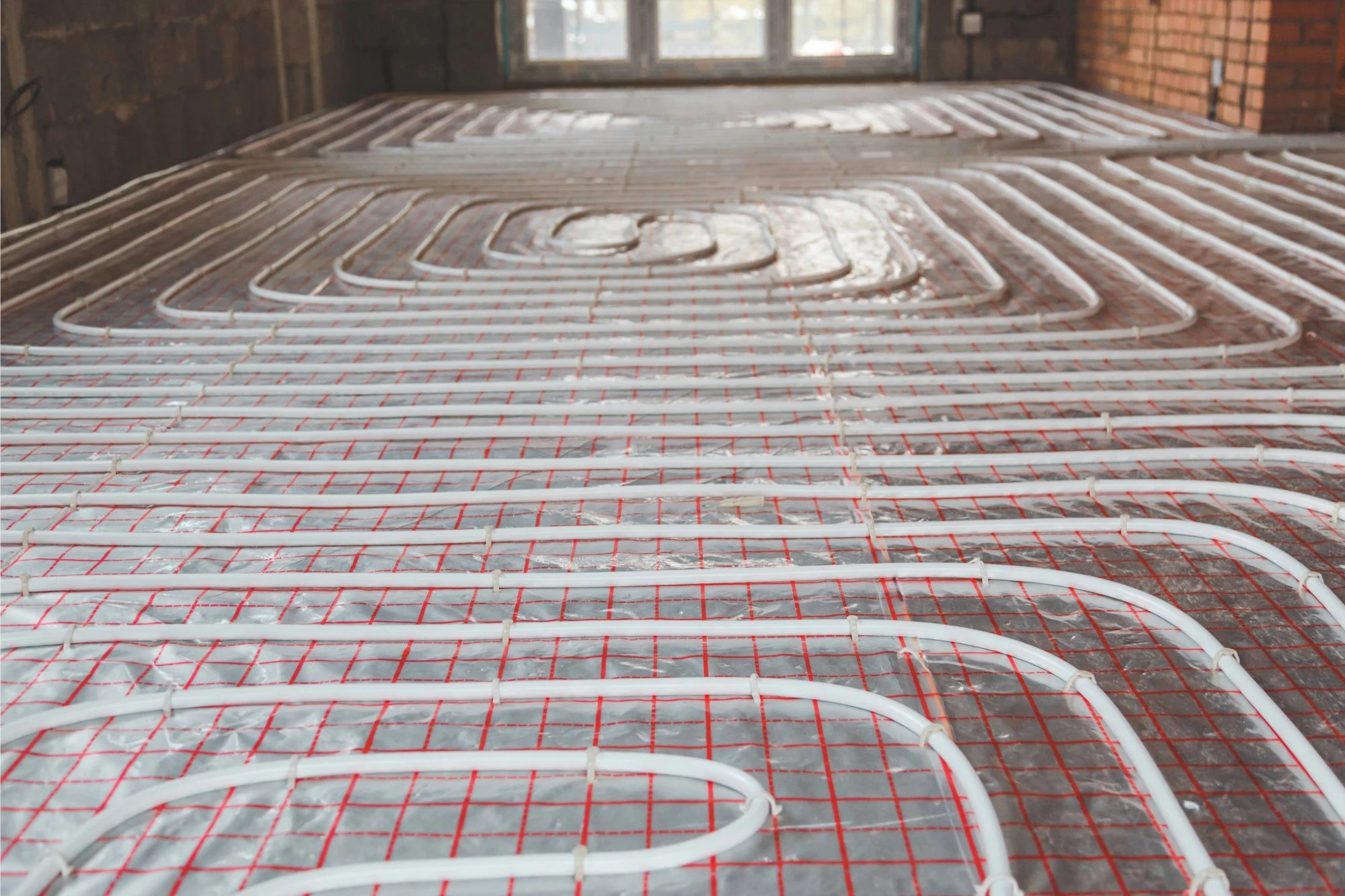 White underfloor heating pipes installed in a coiled pattern over a silver reflective grid.