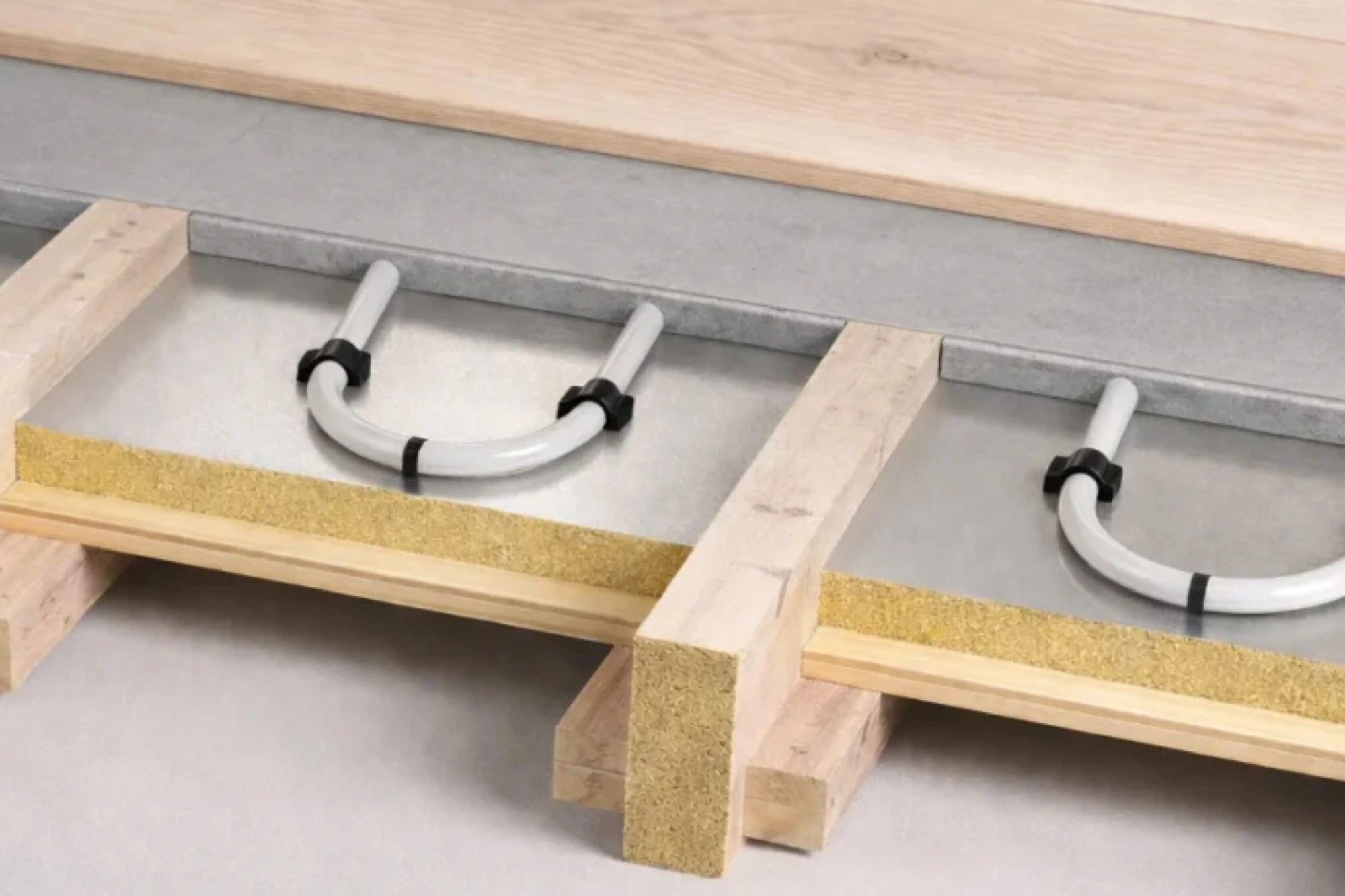 Cross-section diagram of a wet underfloor heating system installed between timber floor joists.